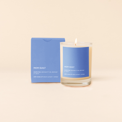 Mom Guilt Candle with blue label and packaging on a beige background