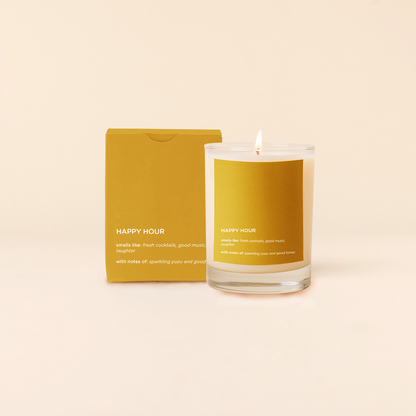 Candle labeled 'Happy Hour' with a matching yellow box on a beige background
