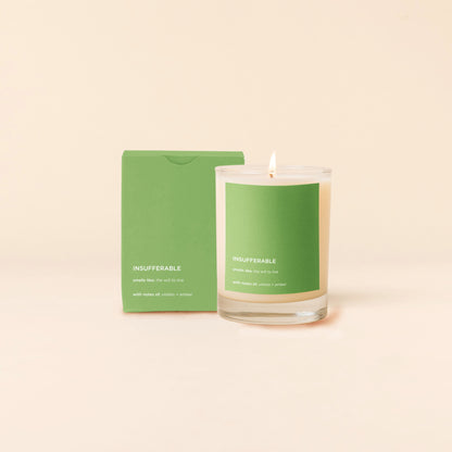 Insufferable Candle with green label and matching green packaging on a beige background