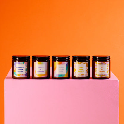 Five jars with colorful labels on a pink platform against an orange background