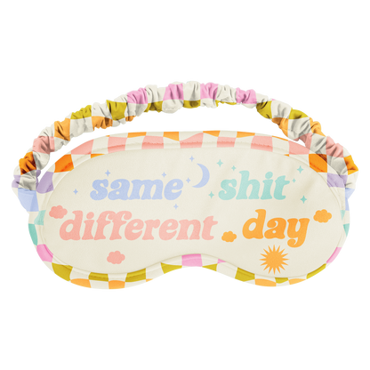 Sleep mask with colorful checkered pattern and text 'same shit different day' on a white background