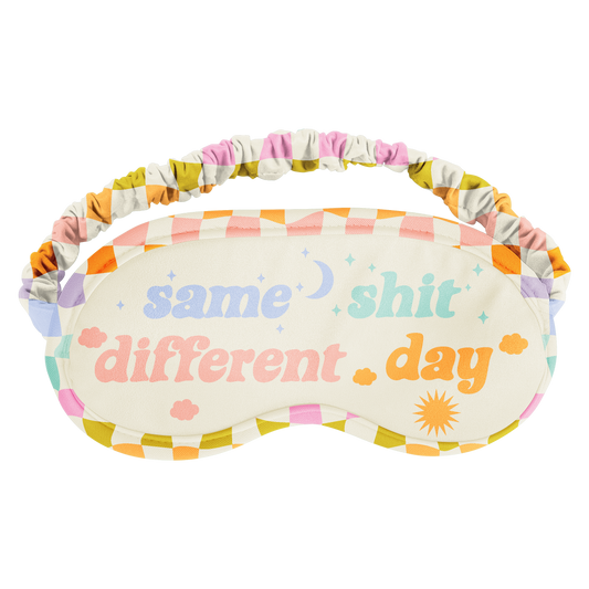 Sleep mask with colorful checkered pattern and text 'same shit different day' on a white background