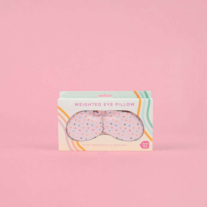Weighted eye pillow packaging with colorful design on a pink background