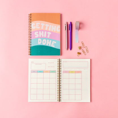 Colorful planner with 'GETTING SHIT DONE' cover on a pink background