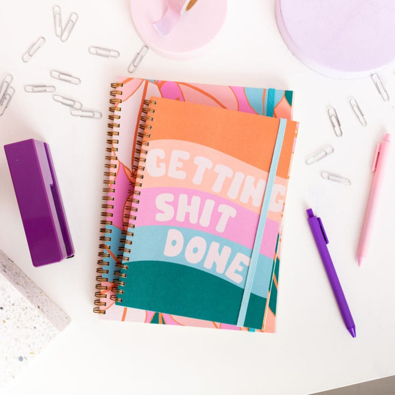 Colorful notebook with 'GETTING SHIT DONE' text on a desk with stationery items.