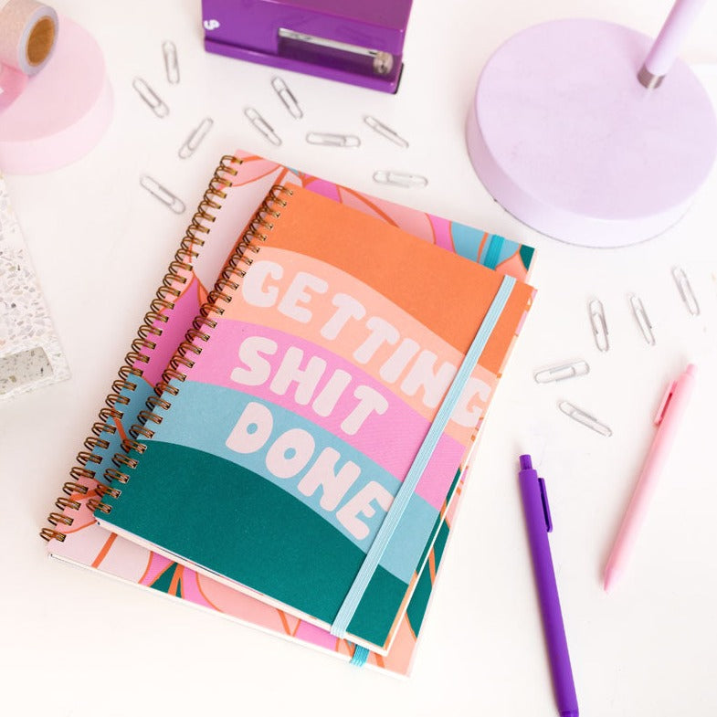 Colorful notebook with 'GETTING SHIT DONE' text on a desk with office supplies.