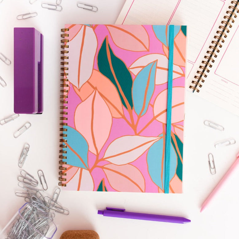 Notebook with colorful leaf pattern surrounded by office supplies on a white background