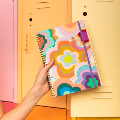 Colorful notebook with floral design held by a hand in front of a yellow locker.
