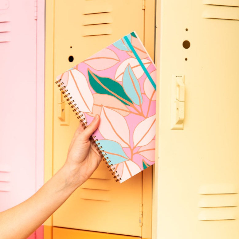 Hand holding a colorful notebook in front of a yellow locker.