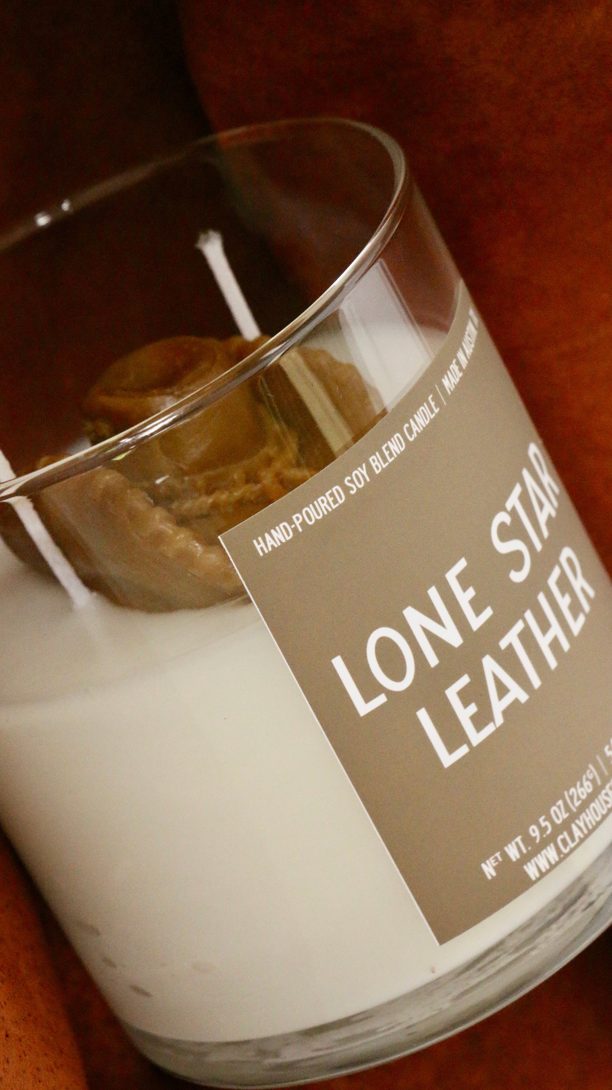 Candle in a glass jar with a label reading 'Lone Star Leather' on a wooden surface.