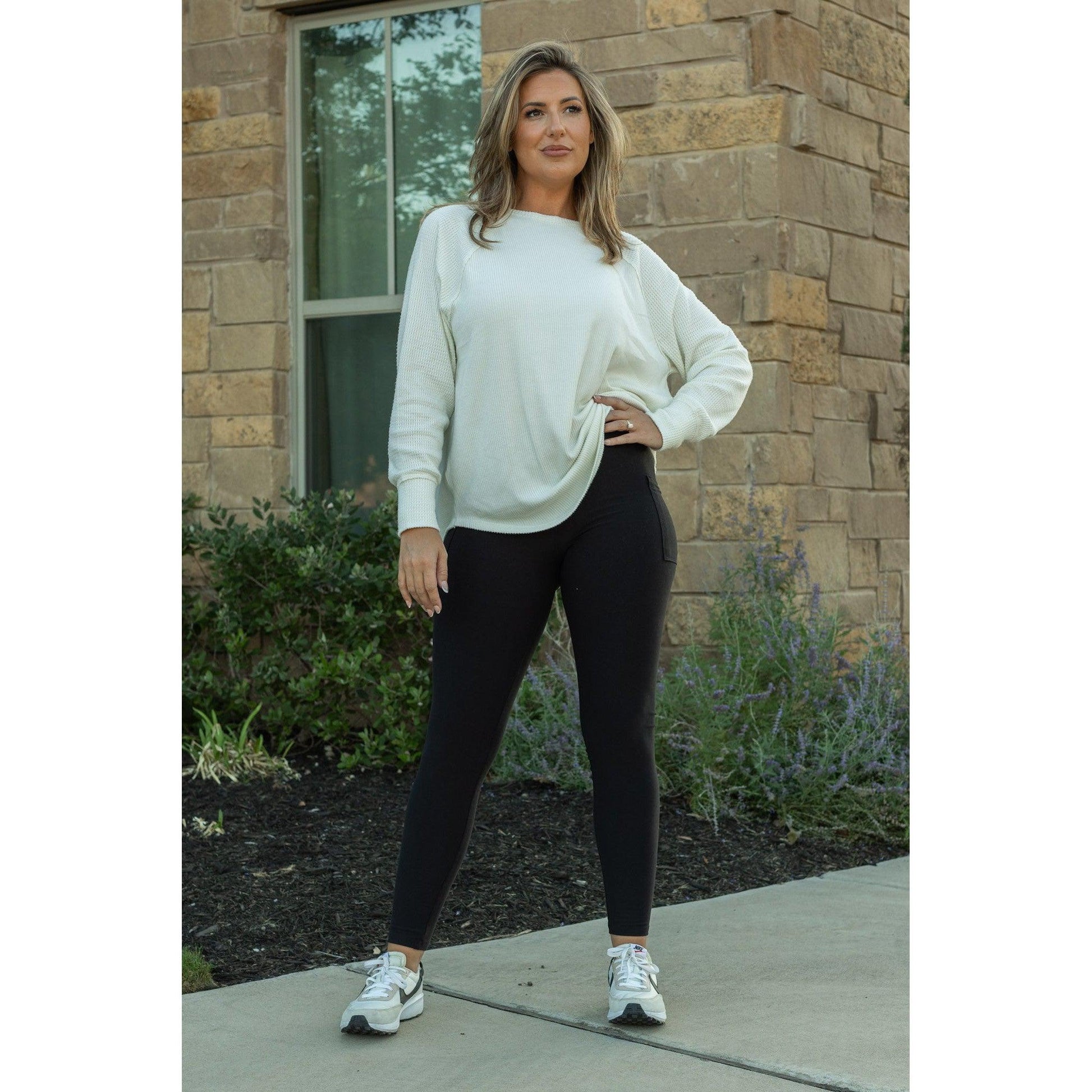 Woman wearing fleece black leggings a white sweater and standing in front of a brick building.