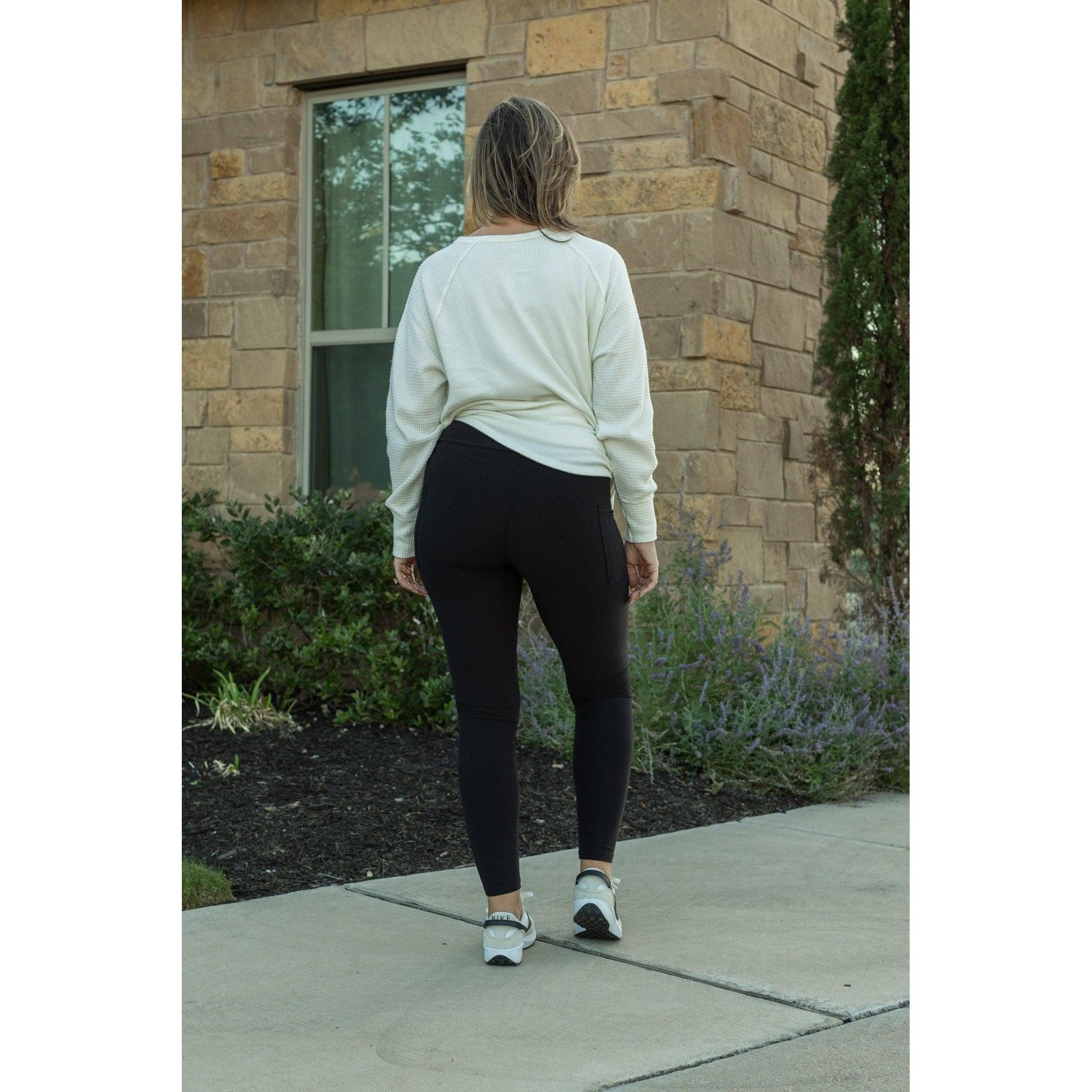 Woman wearing a white sweatshirt and black leggings standing on a sidewalk.