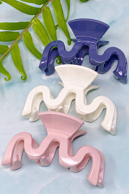 Three wavy wave hair clips in purple, white, and pink on a light blue background with green leaves.