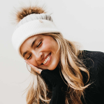 Woman wearing a white beanie with a fluffy pom-pom on a light background