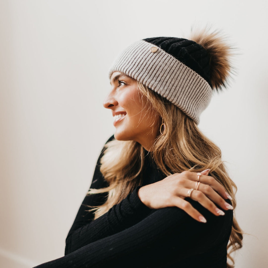 Woman wearing a two-tone beanie with a pom-pom on a plain background