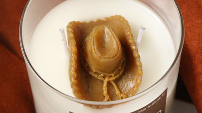 Candle with a boot-shaped wick inside a glass container on a brown background