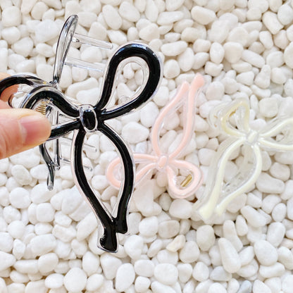 Black bow-shaped hair clip held by a hand on a white pebble background