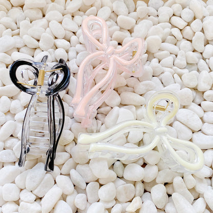Three hair clips in black, pink, and white on a white pebble background