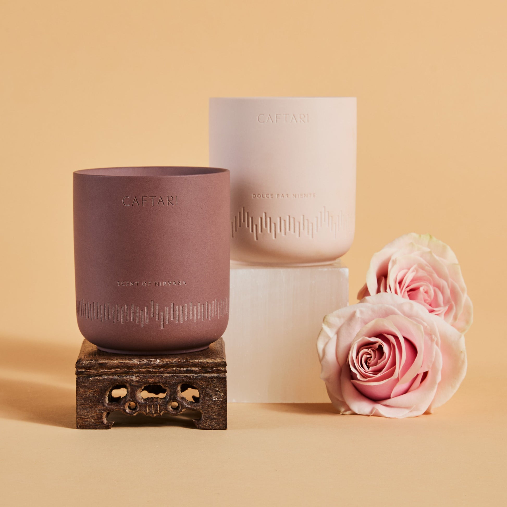 Two ceramic cups with 'CAFTARI' branding, one on a stand, the other stacked, with pink roses on a beige background.