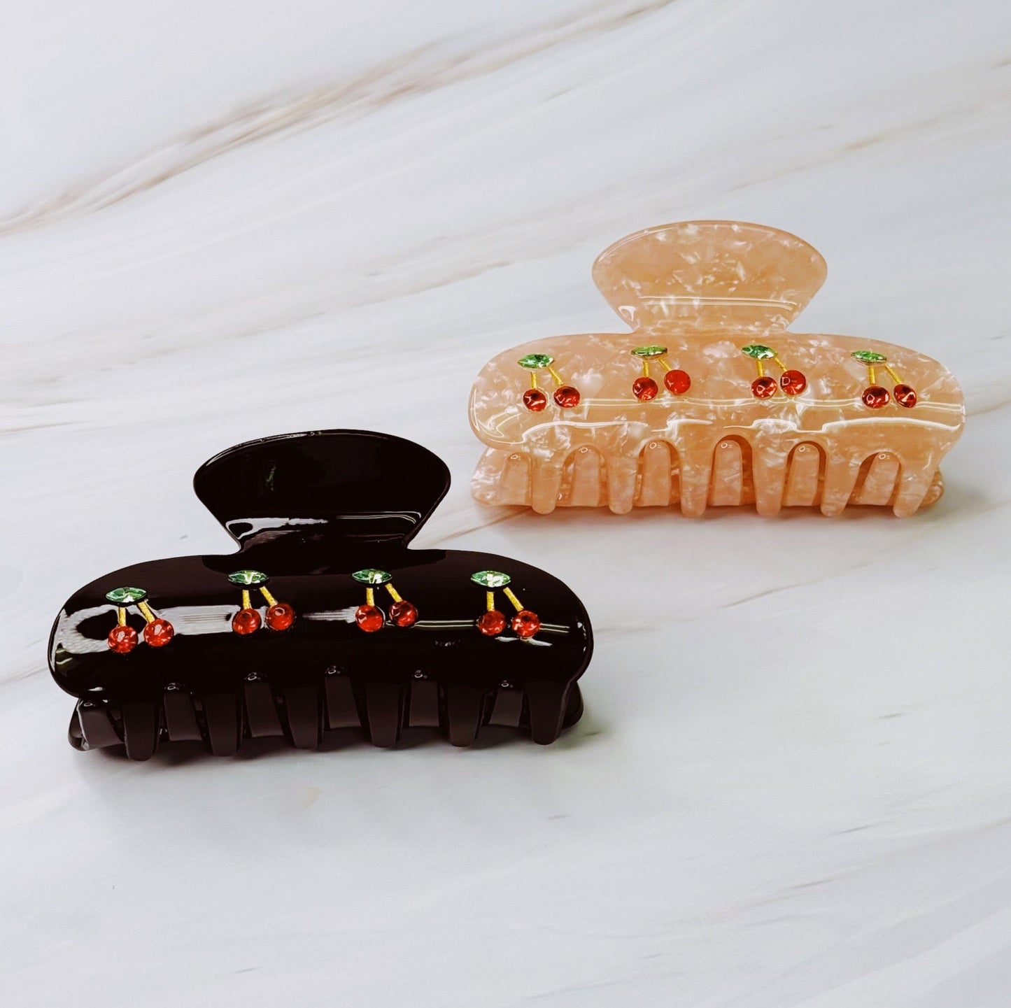 Two hair clips, one black and one peach-colored, with decorative elements on a white surface.