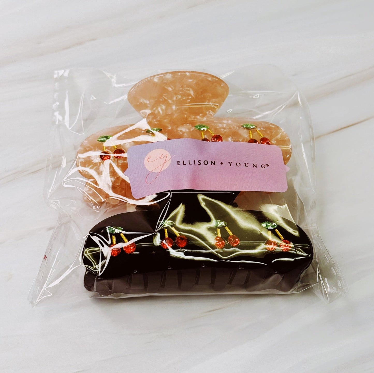 Two hairclips with cherry design in clear packaging with a visible brand label on a light surface.