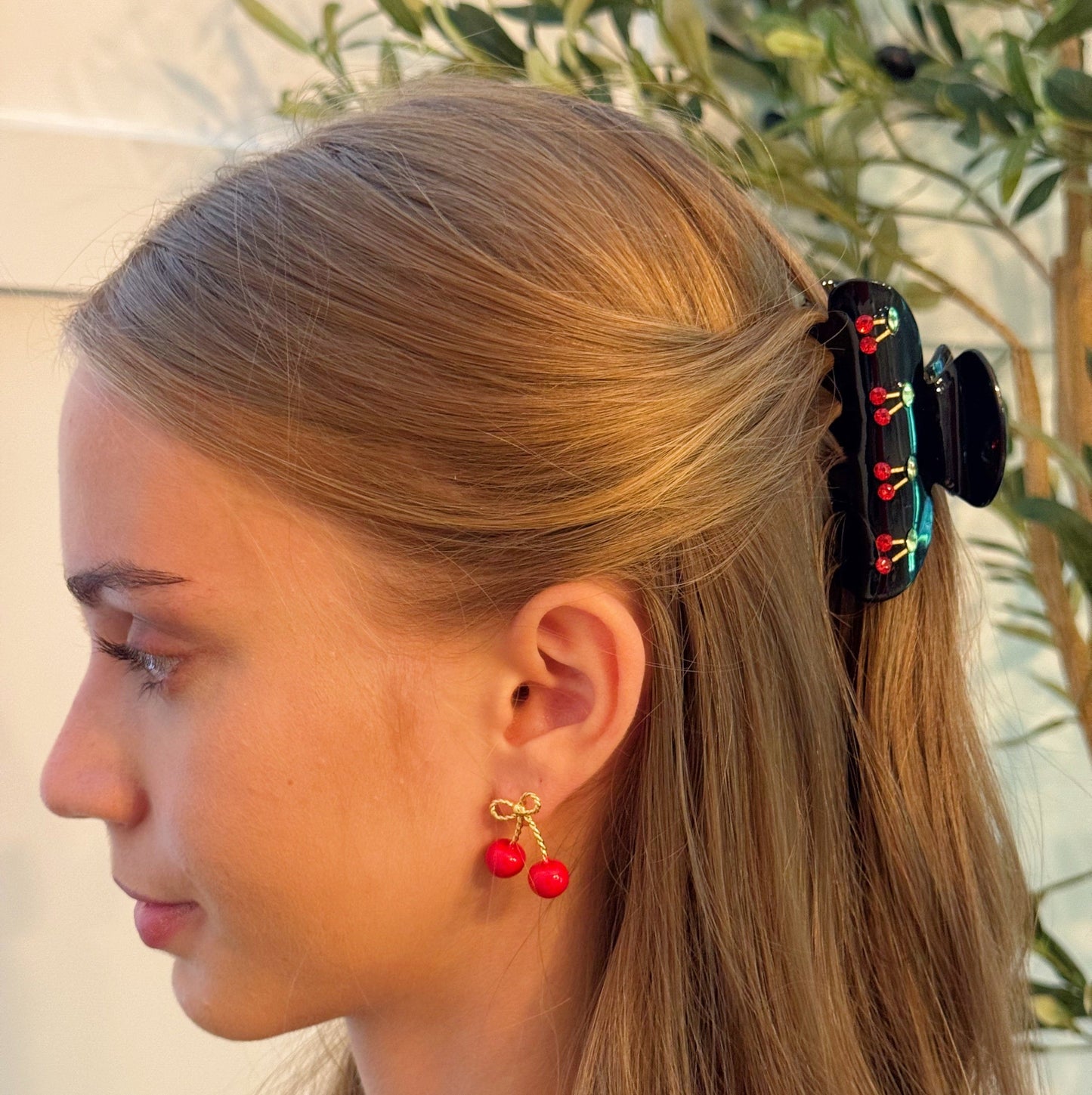 Woman with a ponytail using a decorative hair clip, wearing red cherry earrings.