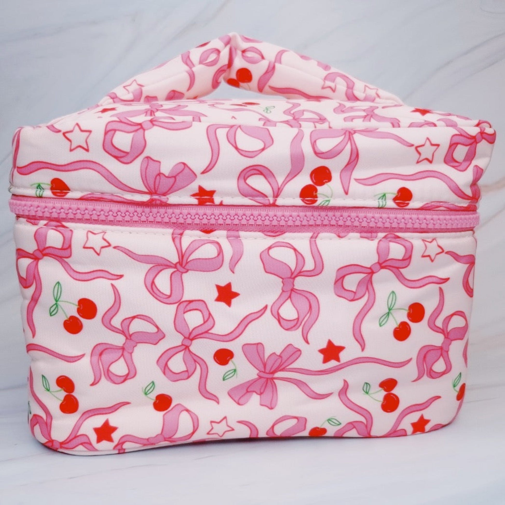 Pink and white cosmetic bag with bow and cherry pattern on a light gray background