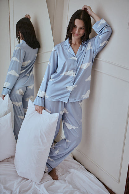 Woman wearing a blue pajama set with cloud pattern on a bed.