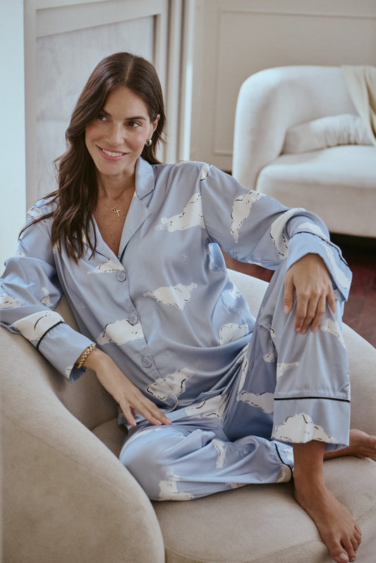 Woman wearing a light blue pajama set with cloud patterns, sitting on a beige armchair.