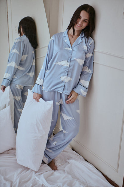 Woman wearing a light blue pajama set with cloud pattern in a bedroom.