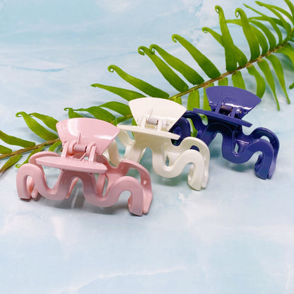 Three wave hair clips in pink, white, and blue on a light blue background with green leaves.