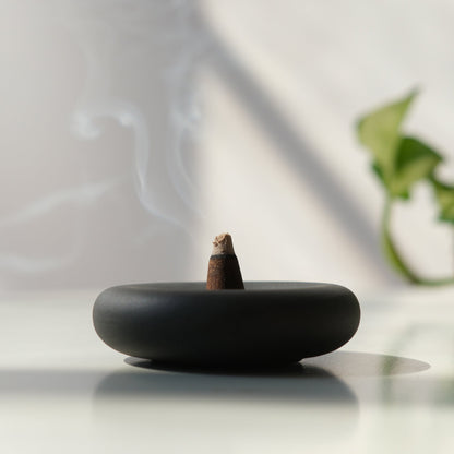 handmade Black incense burner with a smoking incense stick on a light surface.