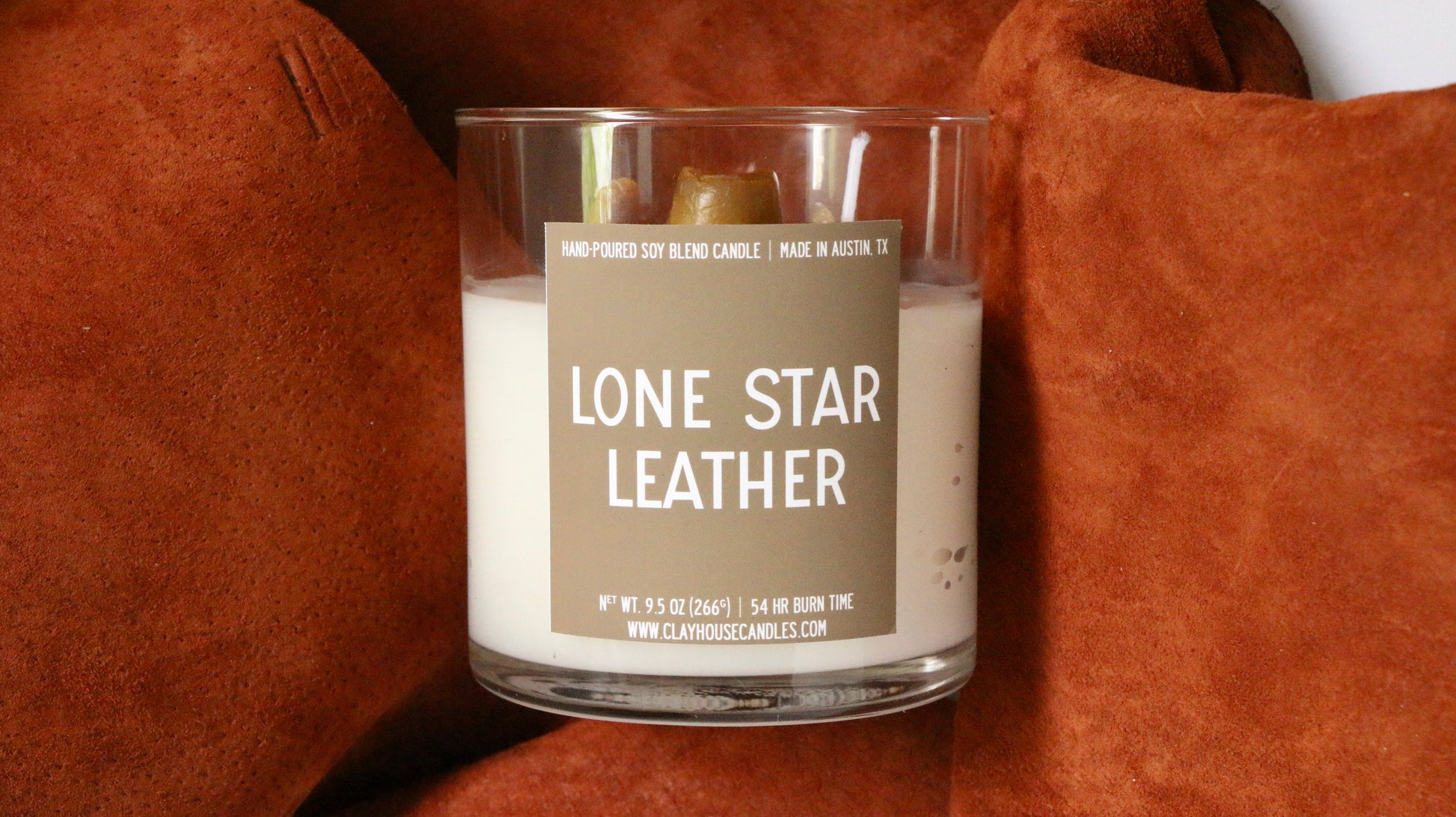 Candle in a glass jar with a label reading 'Lone Star Leather' on a brown textured surface.