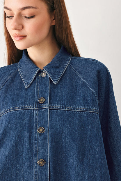 Close-up of a model wearing a blue denim button-up shirt jacket with a pointed collar and decorative metal buttons.