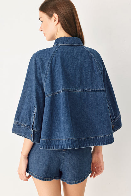A woman shown from the back wearing a cropped blue denim jacket with wide three-quarter sleeves and matching denim shorts, against a plain light background.