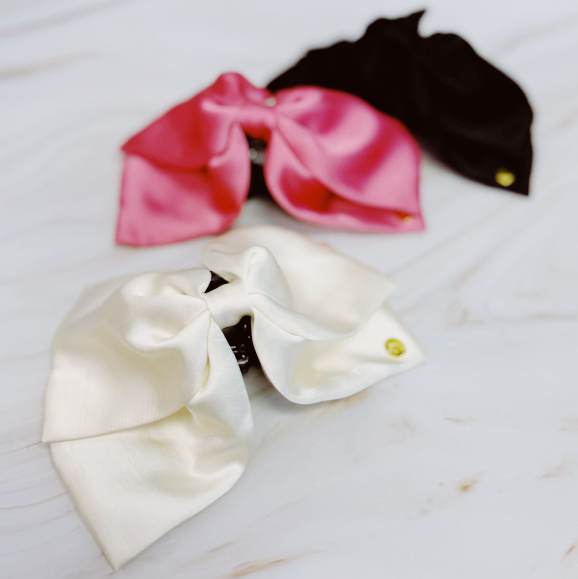 Three satin hair claw in pink, white, and black on a marble surface.