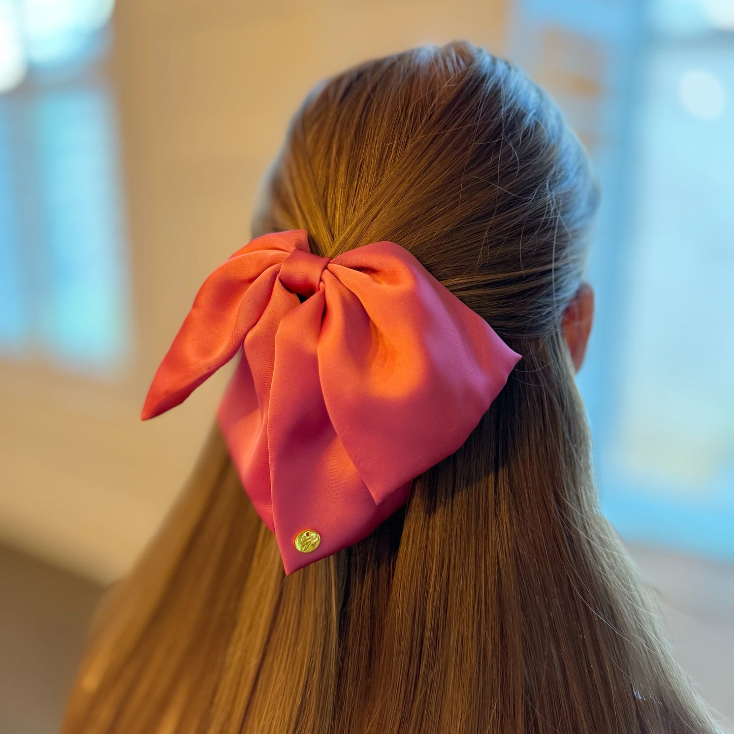 Person with a large pink bow hair claw in their hair against a blurred background