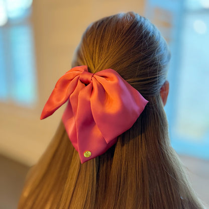 Person with a large pink bow hair claw in their hair against a blurred background