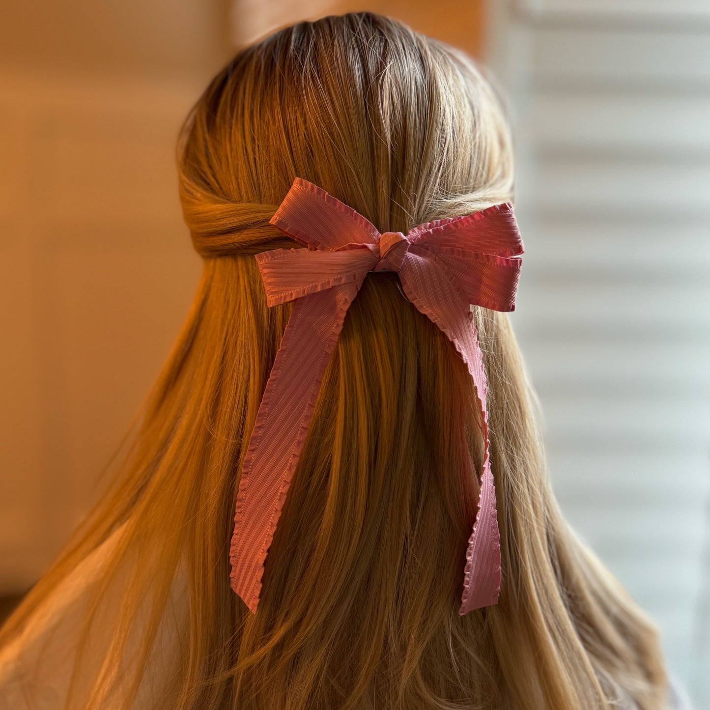 Person with long hair tied back with a large pink bow against a blurred background