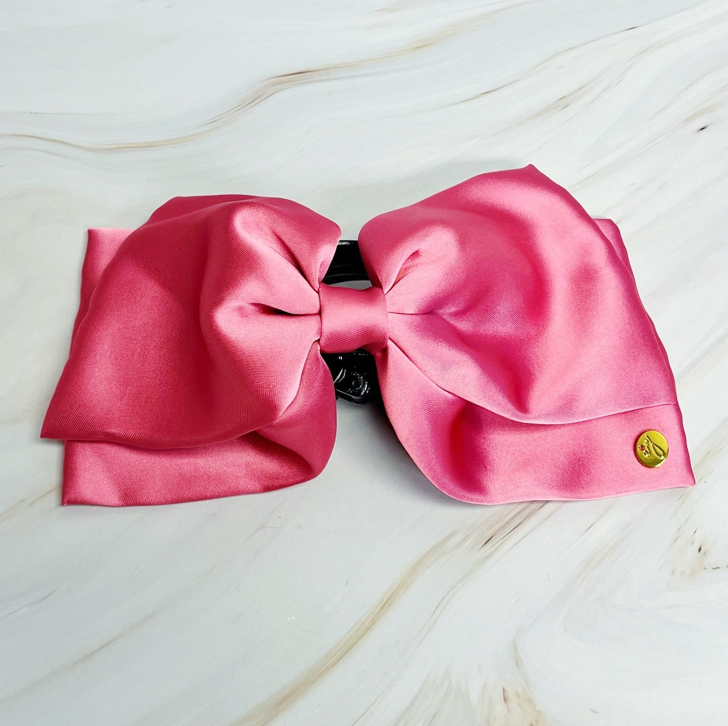 Large pink bow hair claw with a gold emblem on a light wooden surface