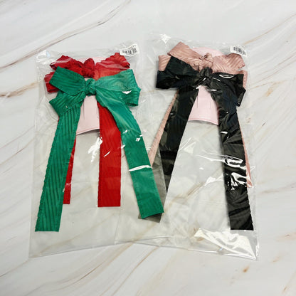 Two large hair clip bows in red, green, and black on a white marble surface.