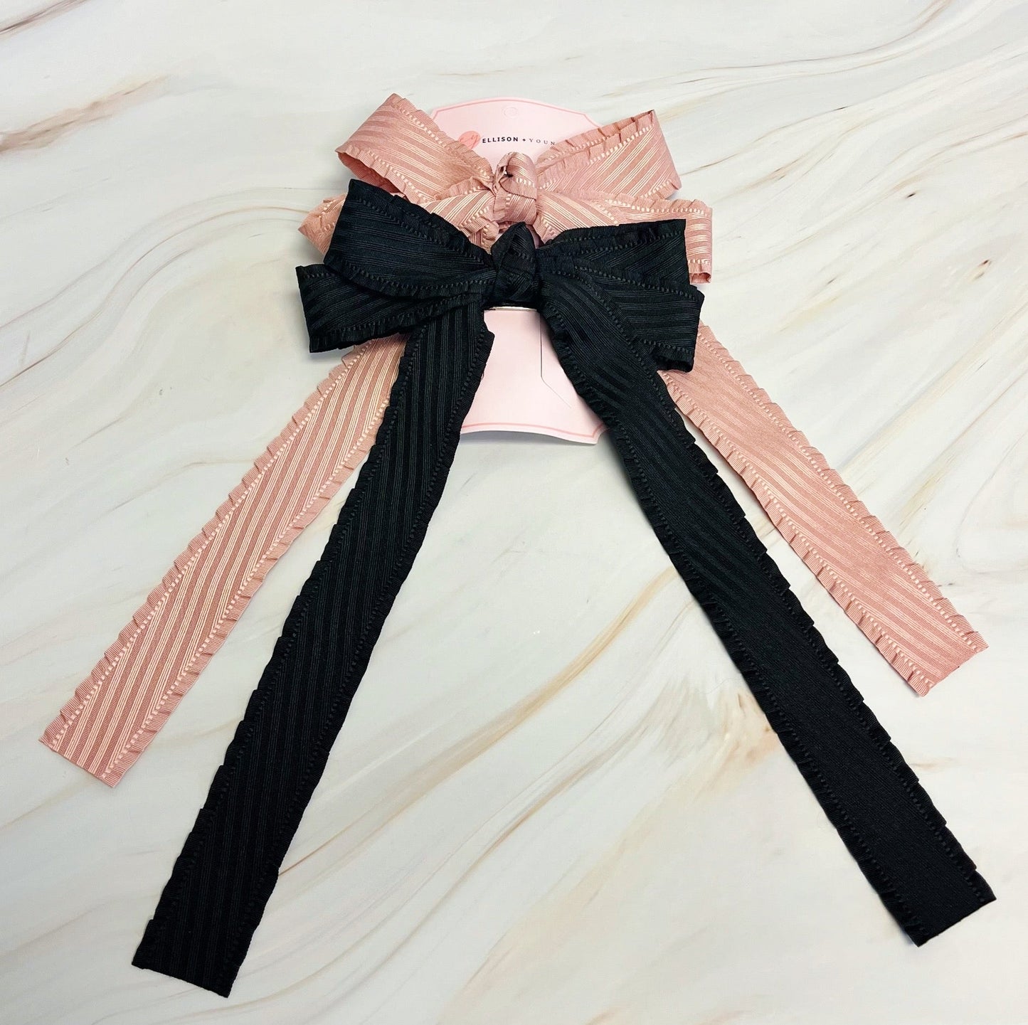 Pink ribbed sweater with a large black bow on a light marble background