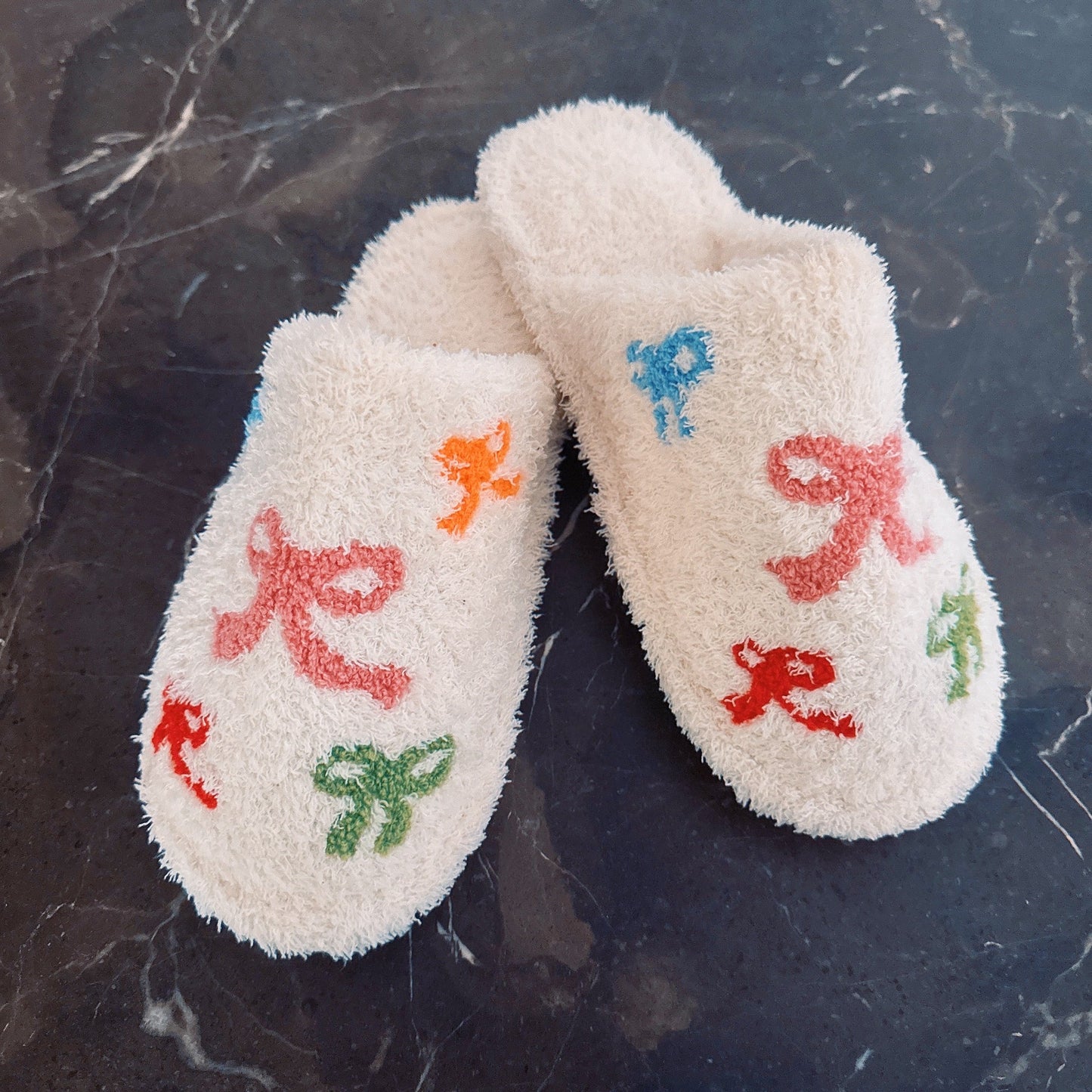 Pair of white slippers with colorful embroidered designs on a dark marble surface
