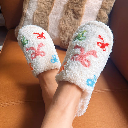White fuzzy socks with colorful designs worn by a person sitting on a brown chair.