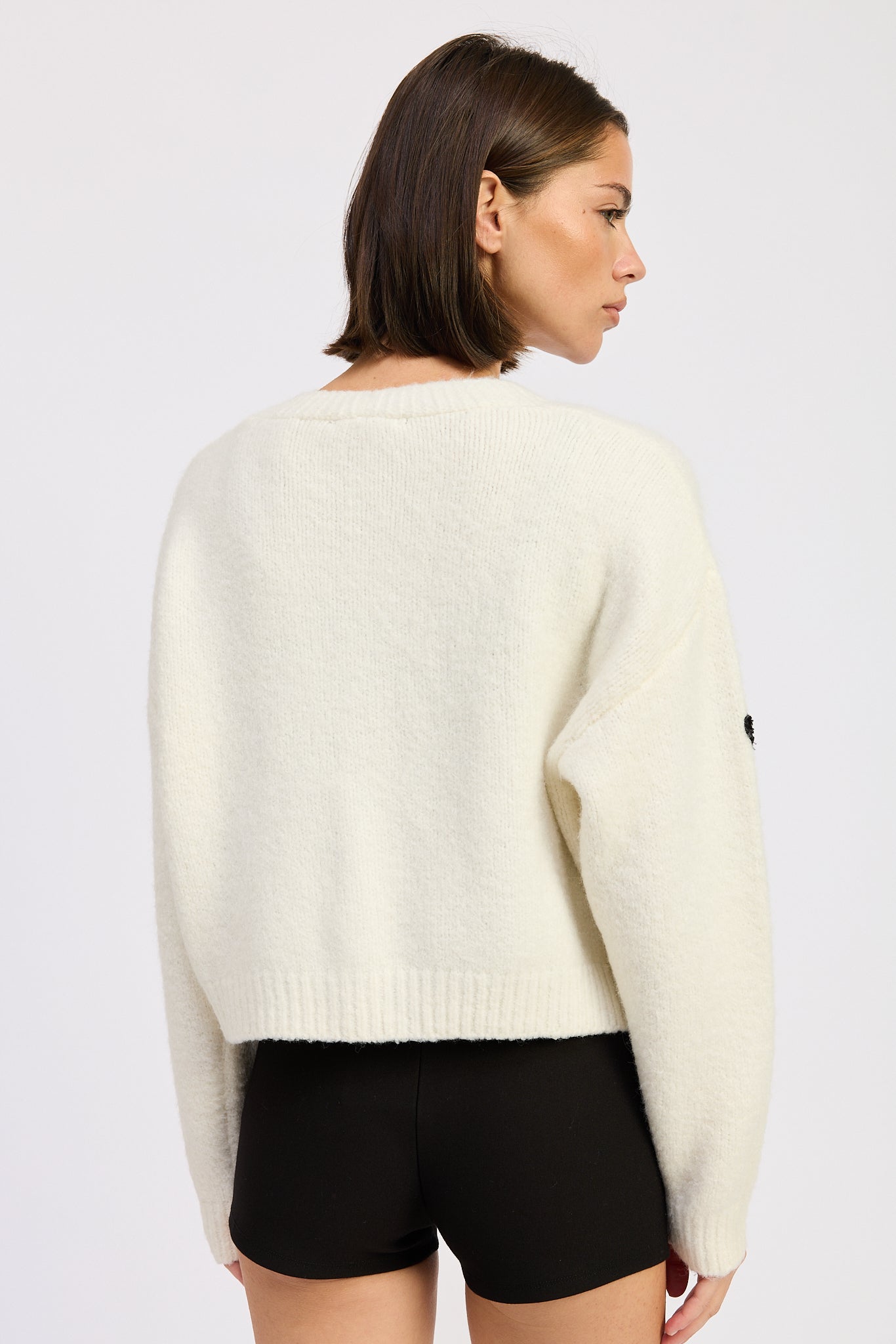Woman wearing a cream sweater and black shorts on a white background
