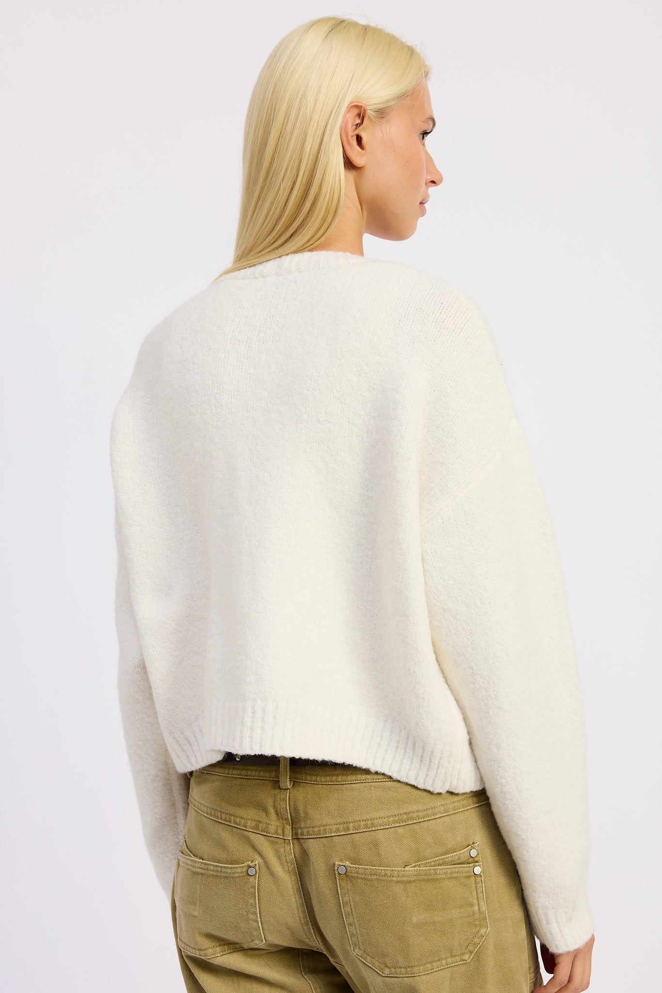 Person wearing a white sweater and green pants on a plain background