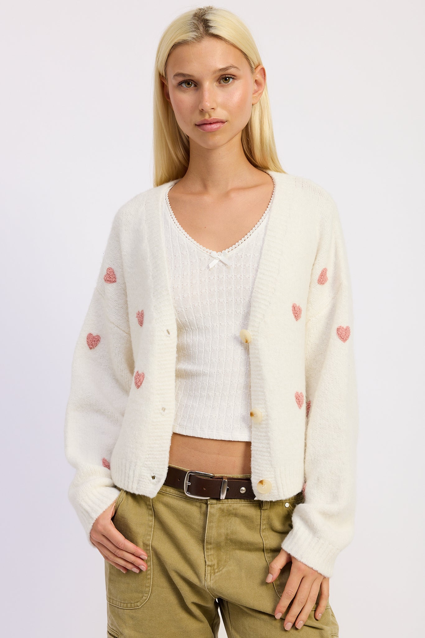 Woman wearing a cream cardigan with heart patterns over a white shirt on a light background