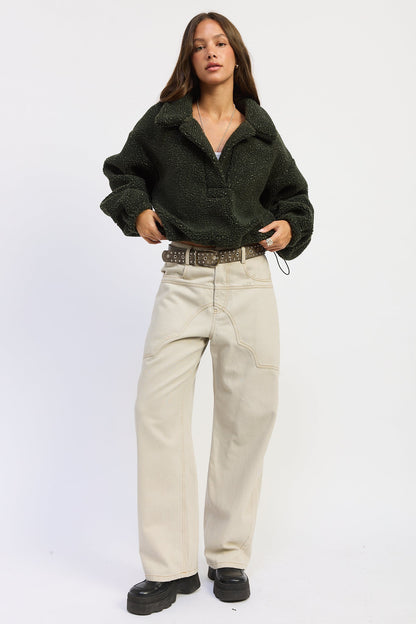 A woman modeling a dark olive green sherpa fleece button-up shirt, paired with beige wide-leg jeans, a brown patterned belt, and black platform shoes, against a plain white studio background.