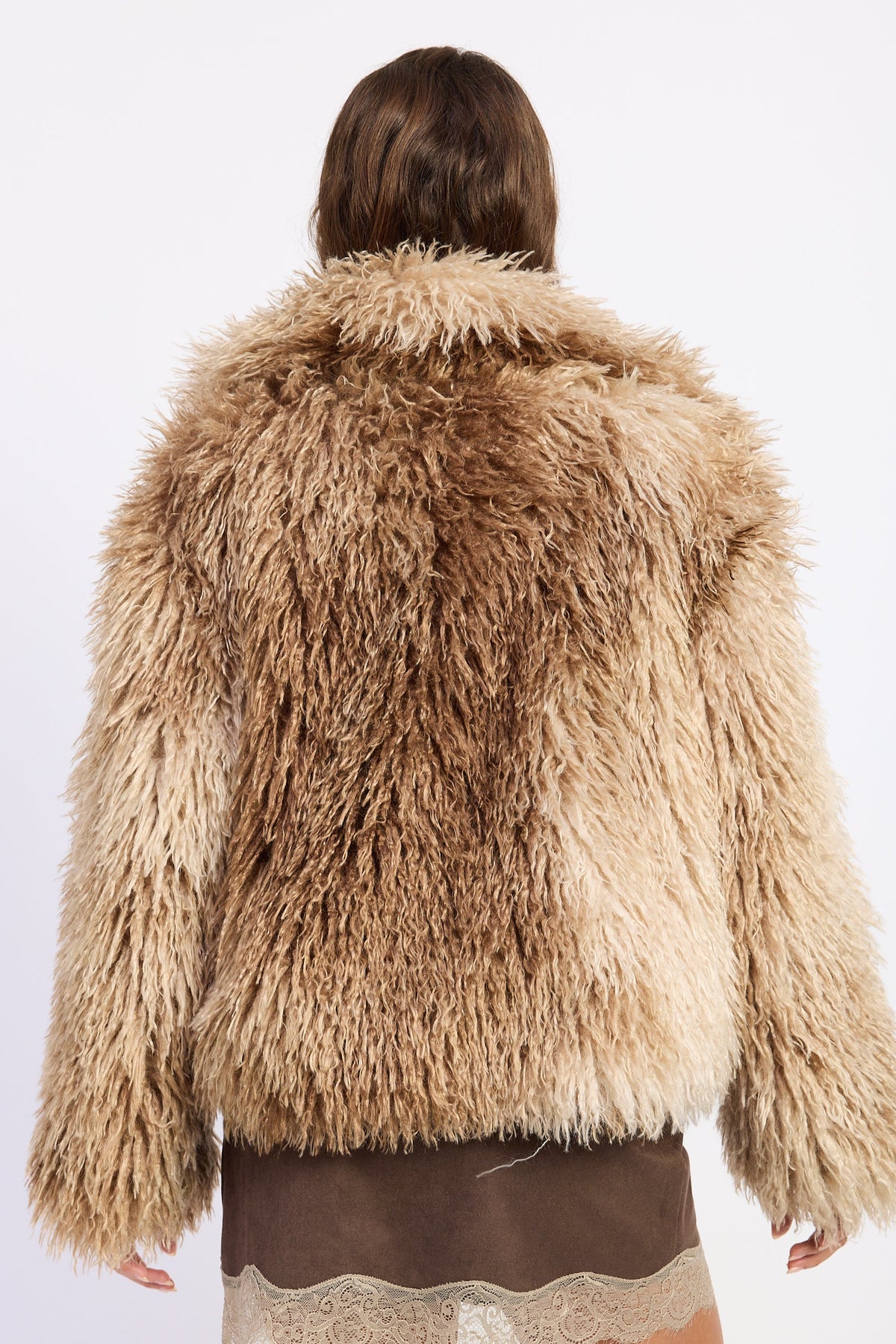 A person viewed from the back wearing a shaggy faux-fur jacket in mixed tan and light brown tones, against a plain light background.