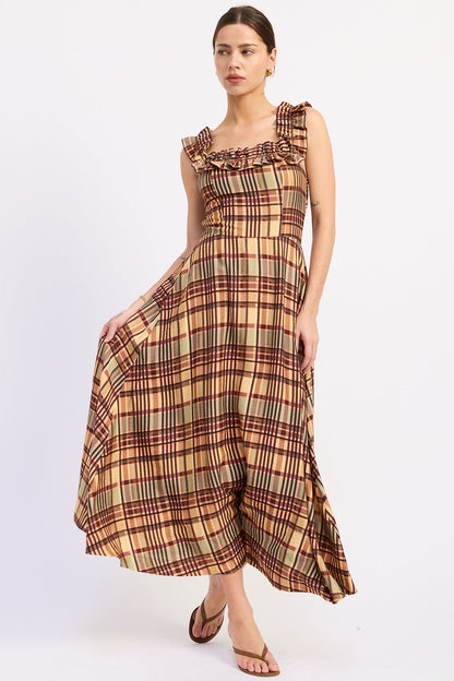 A woman modeling a sleeveless midi dress with a ruffled neckline and a brown, beige, and green plaid pattern, paired with brown flat sandals against a plain white studio background.